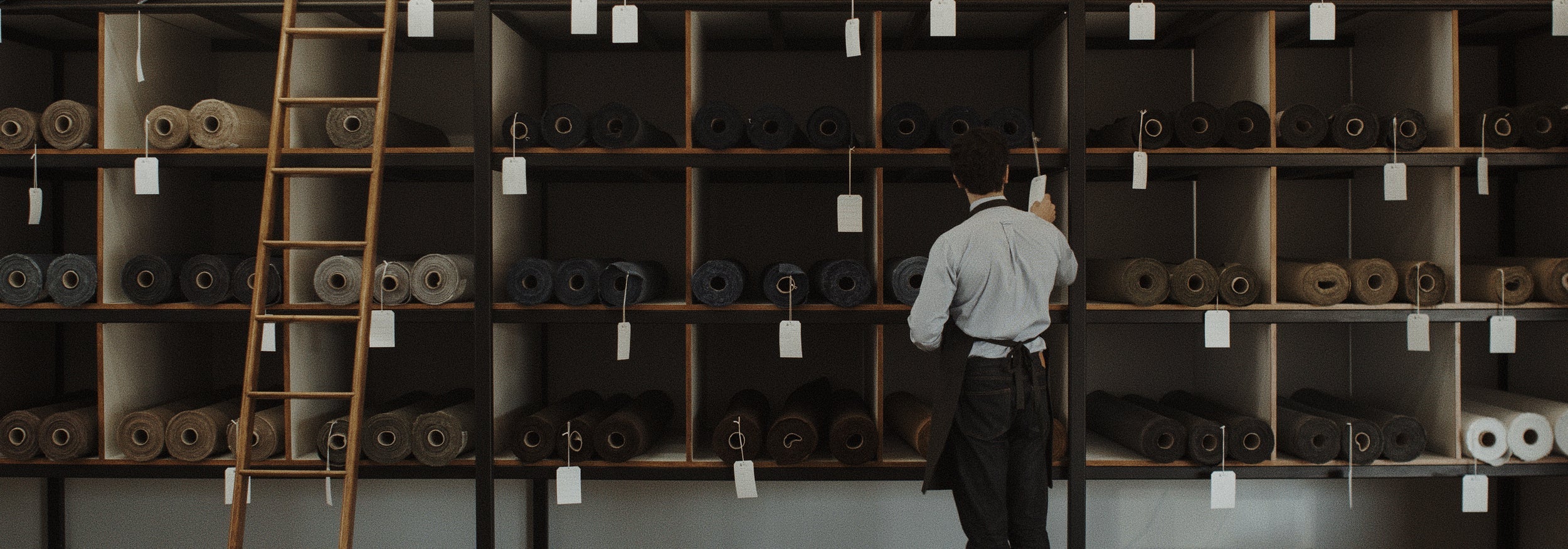 Person standing in front of a large wall of rolls with a ladder on the left.