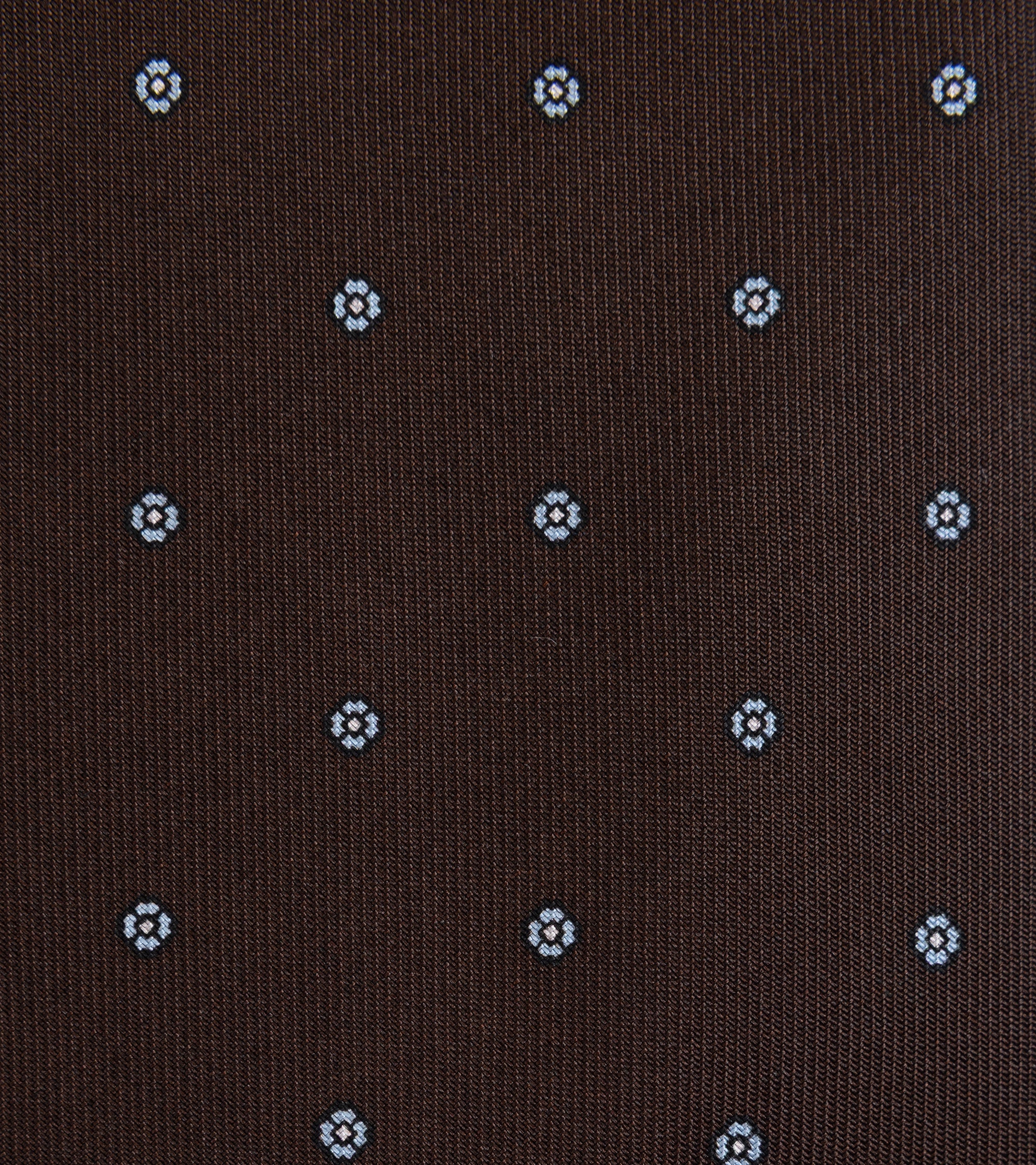 A close-up of a brown woven fabric with a repeating small geometric floral pattern in light blue.