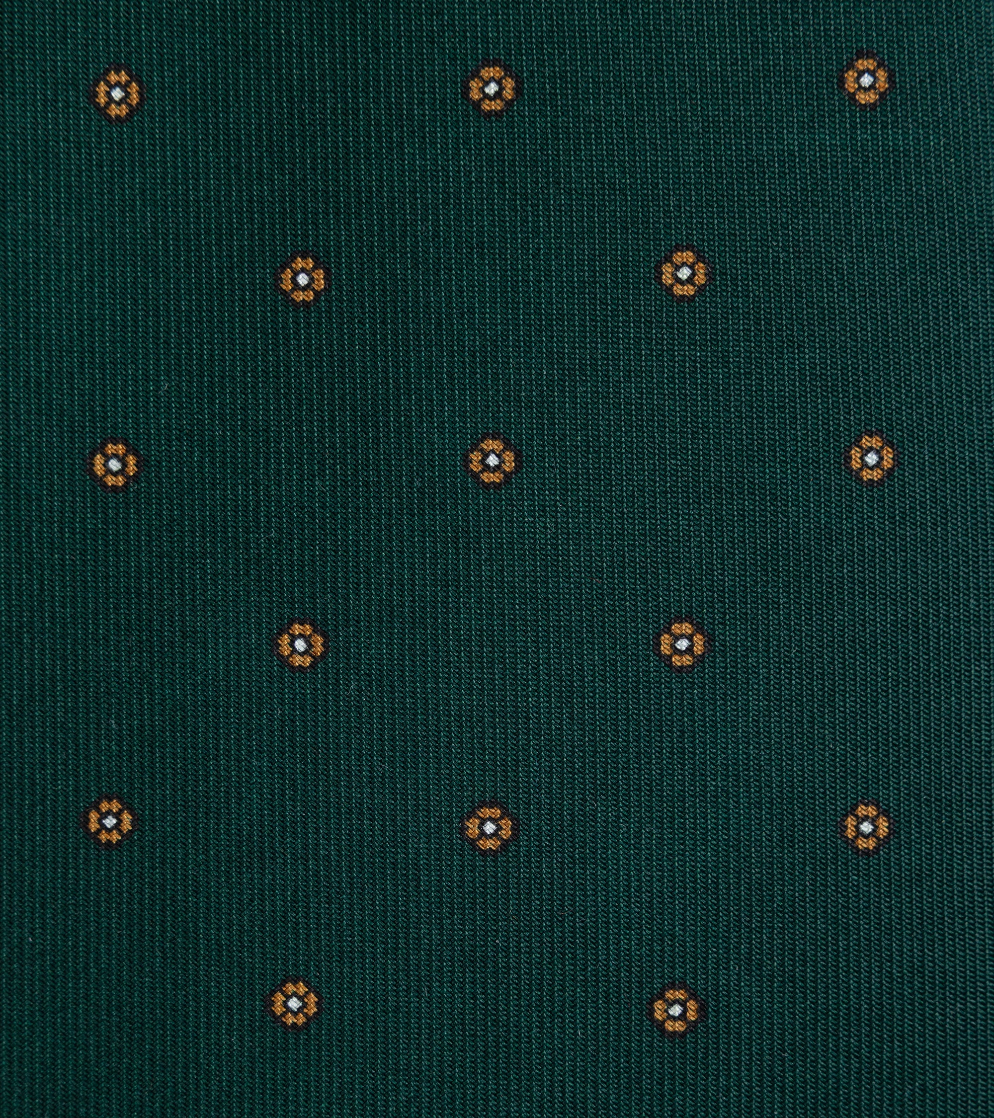 A close-up of a dark green woven fabric with a repeating small geometric floral pattern in orange.