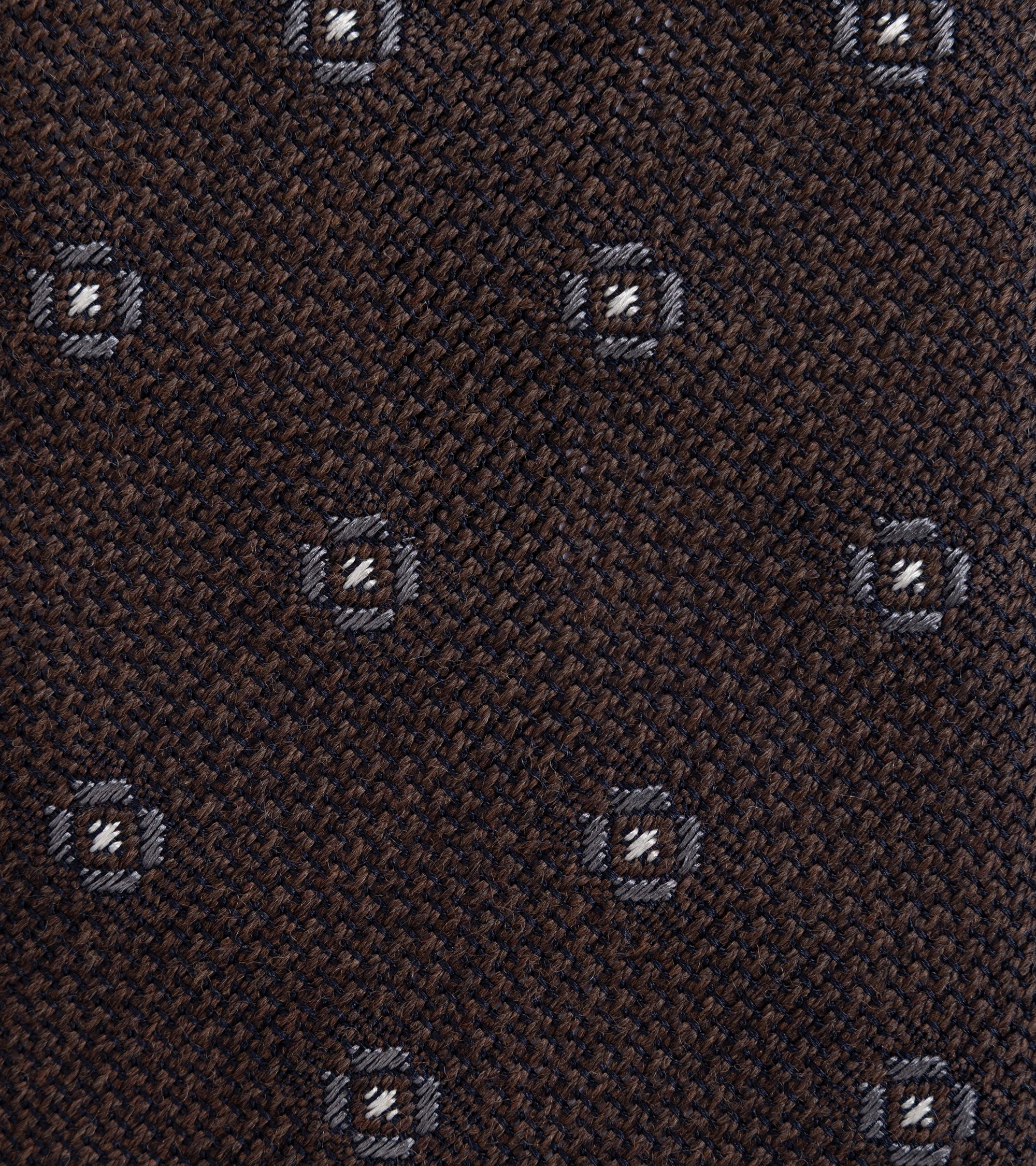 A close-up of a dark brown woven fabric with a repeating small geometric medallion pattern in gray and white.